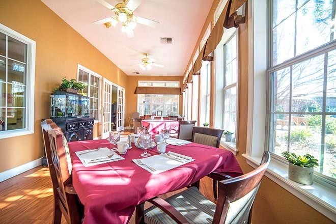 A bright and sunny dining room with a table set for a meal, surrounded by large windows.