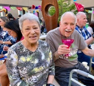 An elderly couple smiling at a social gathering outdoors.