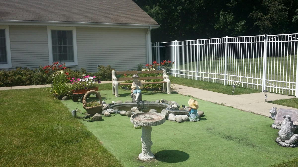 A serene garden with a birdbath, decorative elements, and a fenced yard on a sunny day.