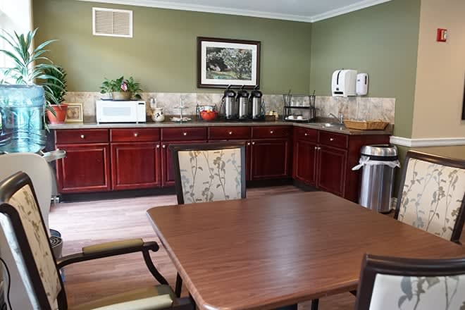 A cozy kitchenette with wooden cabinets, a table and chairs, and a coffee station.