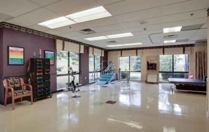 A well-lit gym with various fitness equipment and large windows.