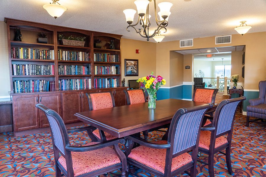 A well-furnished meeting room with a large conference table, bookshelves, and a vase of flowers.