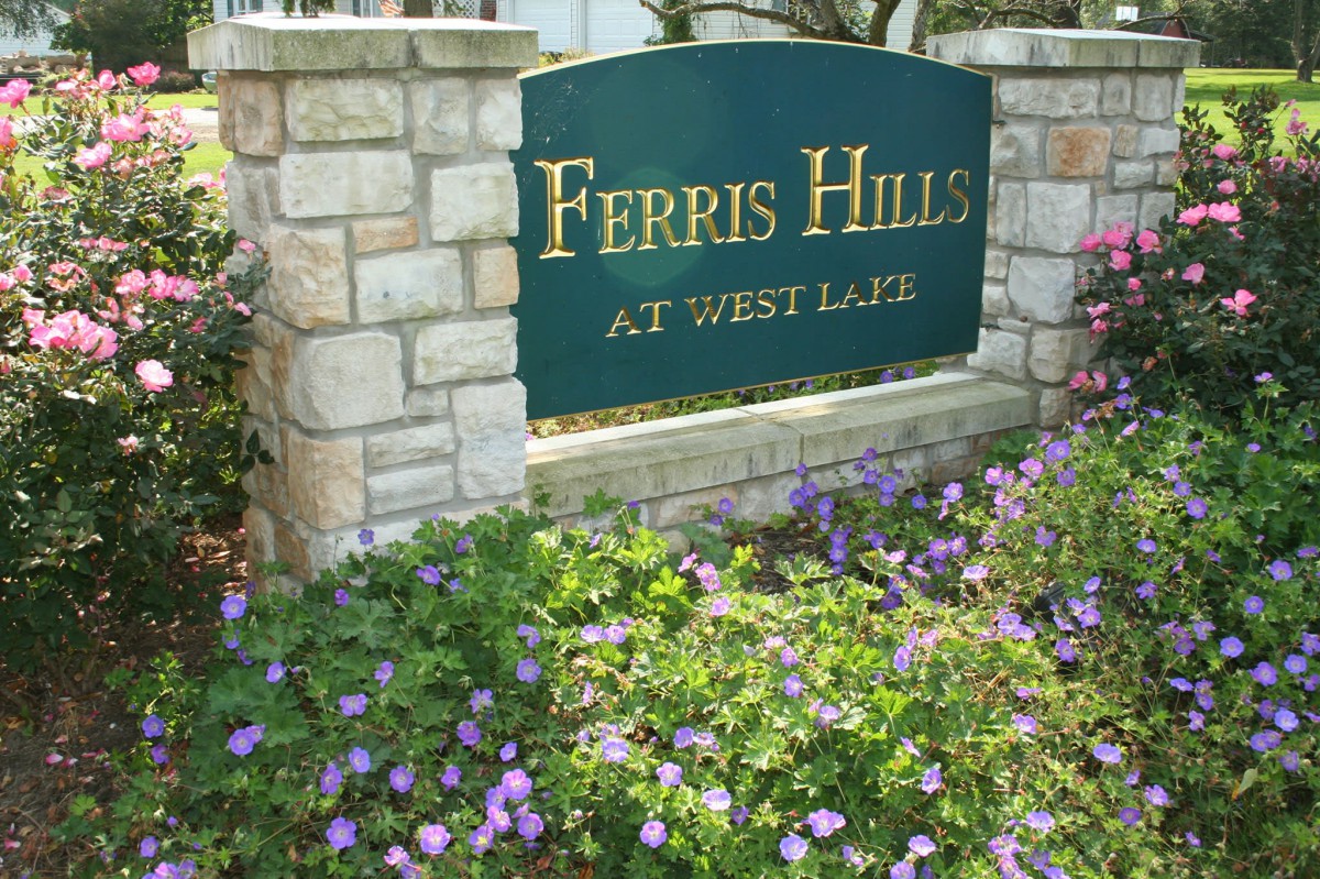 A stone sign for 'Ferris Hills at West Lake' surrounded by blooming flowers.