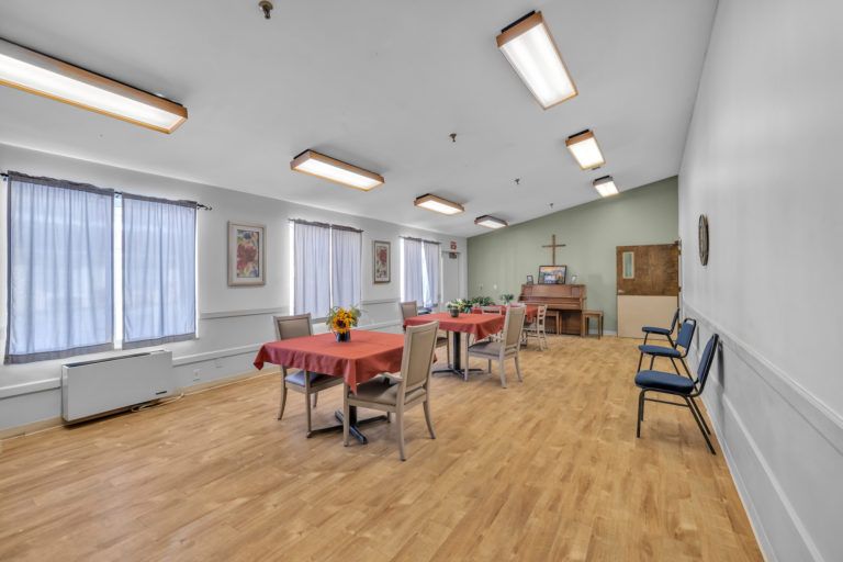 A dining area with neatly arranged tables and chairs, large windows, and bright lighting.
