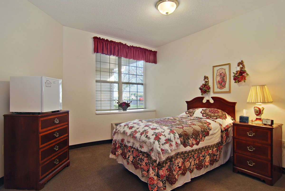 A traditional bedroom with a single bed, floral bedding, and a dresser under a curtained window.