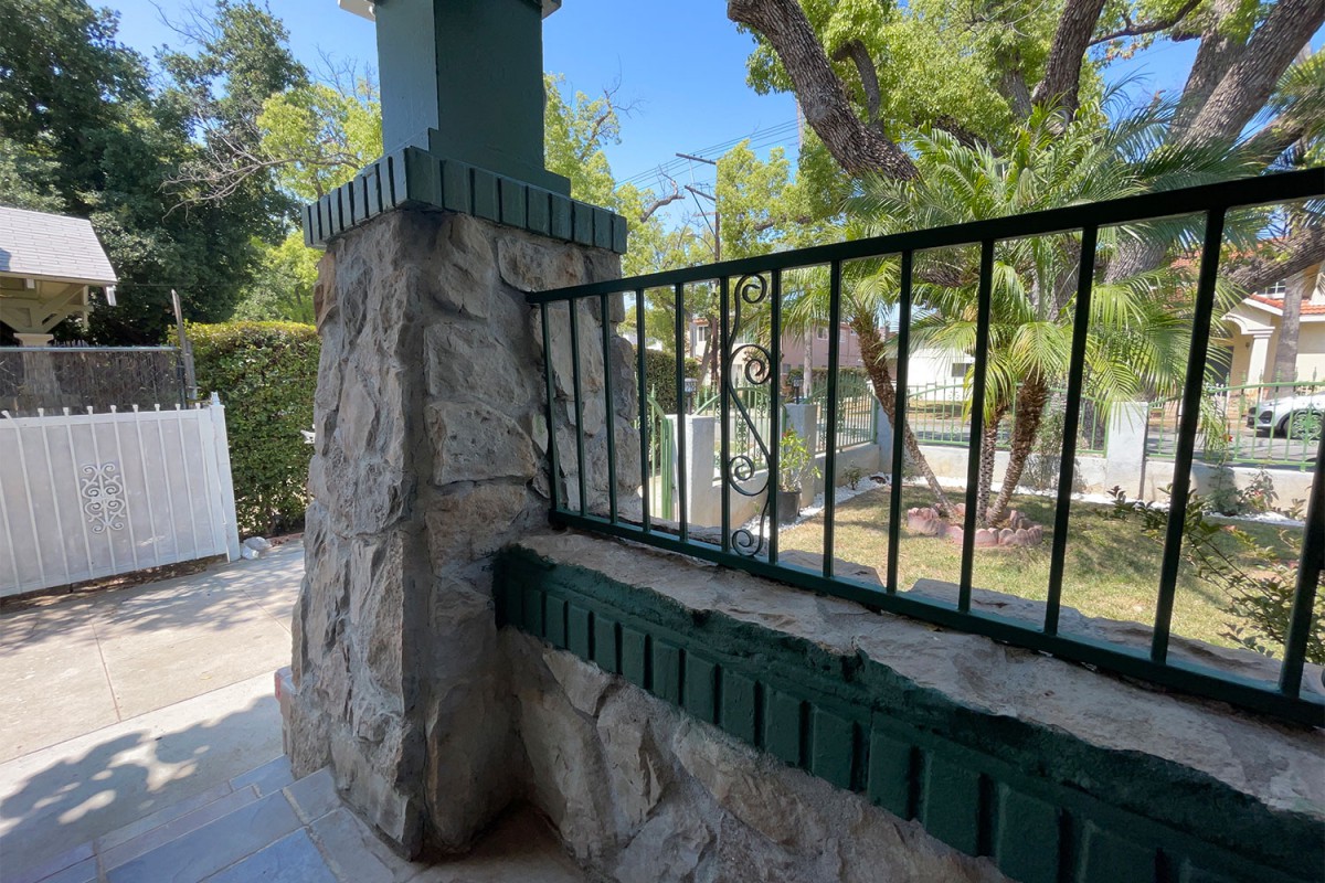 A stone pillar with an iron railing overlooks a sunny garden area.