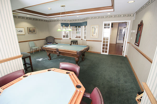 A cozy game room with a pool table and card table, featuring carpet flooring and elegant lighting.