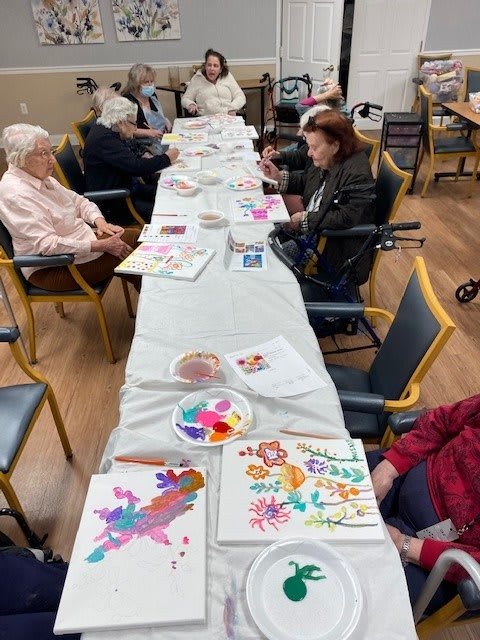 Seniors participate in a lively painting session at a long table.