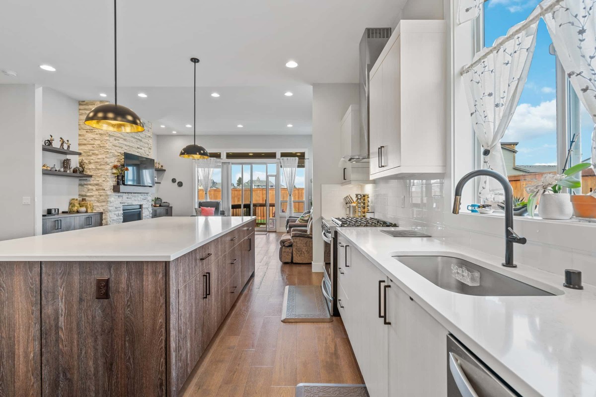 A modern kitchen featuring white cabinetry, a large island with pendant lighting, and wood flooring.