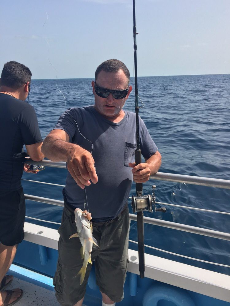 A man holding a fishing rod on a boat in the ocean, having just caught a fish.