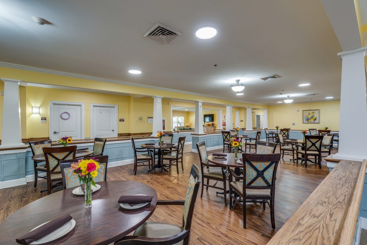 A spacious dining room with neatly arranged tables and chairs, featuring warm lighting and floral decorations.