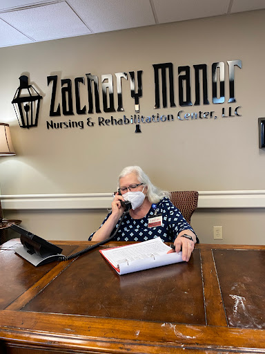 A receptionist at Zachary Manor Nursing & Rehabilitation Center assists a caller while adhering to health protocols.