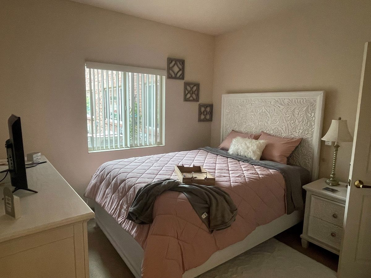 A cozy bedroom with soft pink bedding and natural daylight.