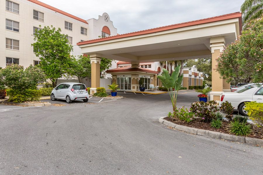 A hotel entrance featuring a driveway with a parked car and surrounding landscaping.