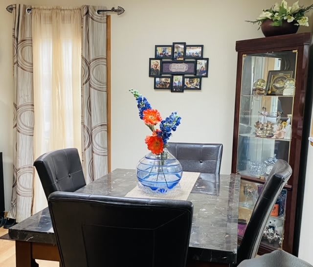 A cozy dining room featuring a table with a decorative vase and flowers, surrounded by chairs and adorned with wall picture frames.