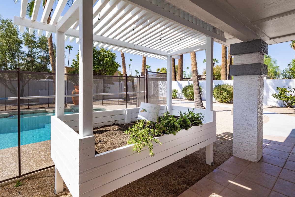 An outdoor garden planter under a pergola in a sunny backyard.