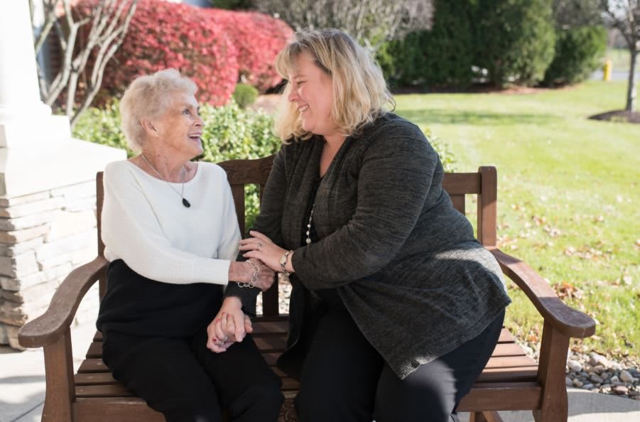 Two women enjoying a conversation on a bench in a garden.