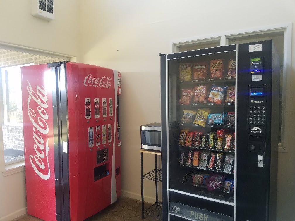 A room with a Coca-Cola vending machine, a snack vending machine, and a microwave.