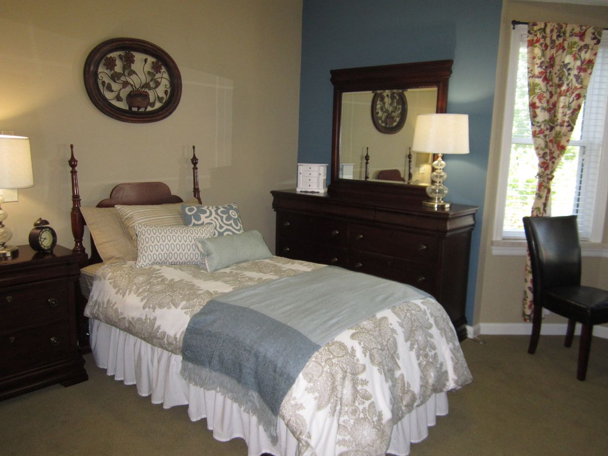 A cozy bedroom with a single bed and a wooden dresser beside a window.