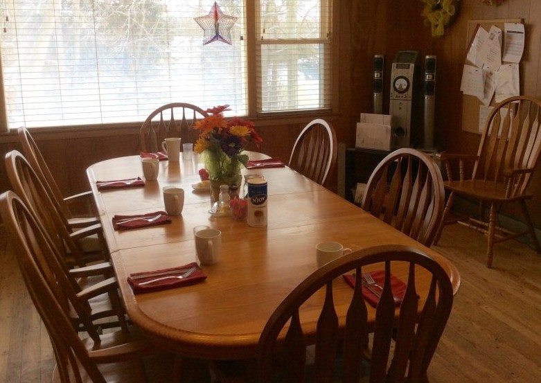 A cozy dining room with a wooden table set for breakfast, featuring flowers as a centerpiece.