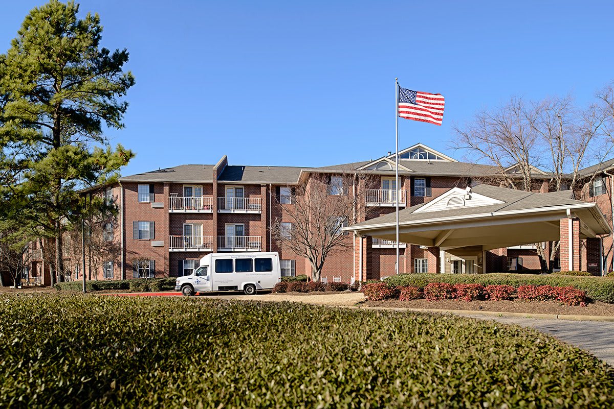 A brick building with a transport van parked nearby and an American flag flying under a clear blue sky.