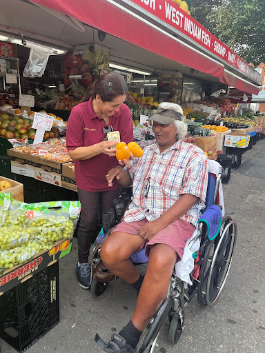 A friendly interaction at a local market, where a vendor helps a customer in a wheelchair.