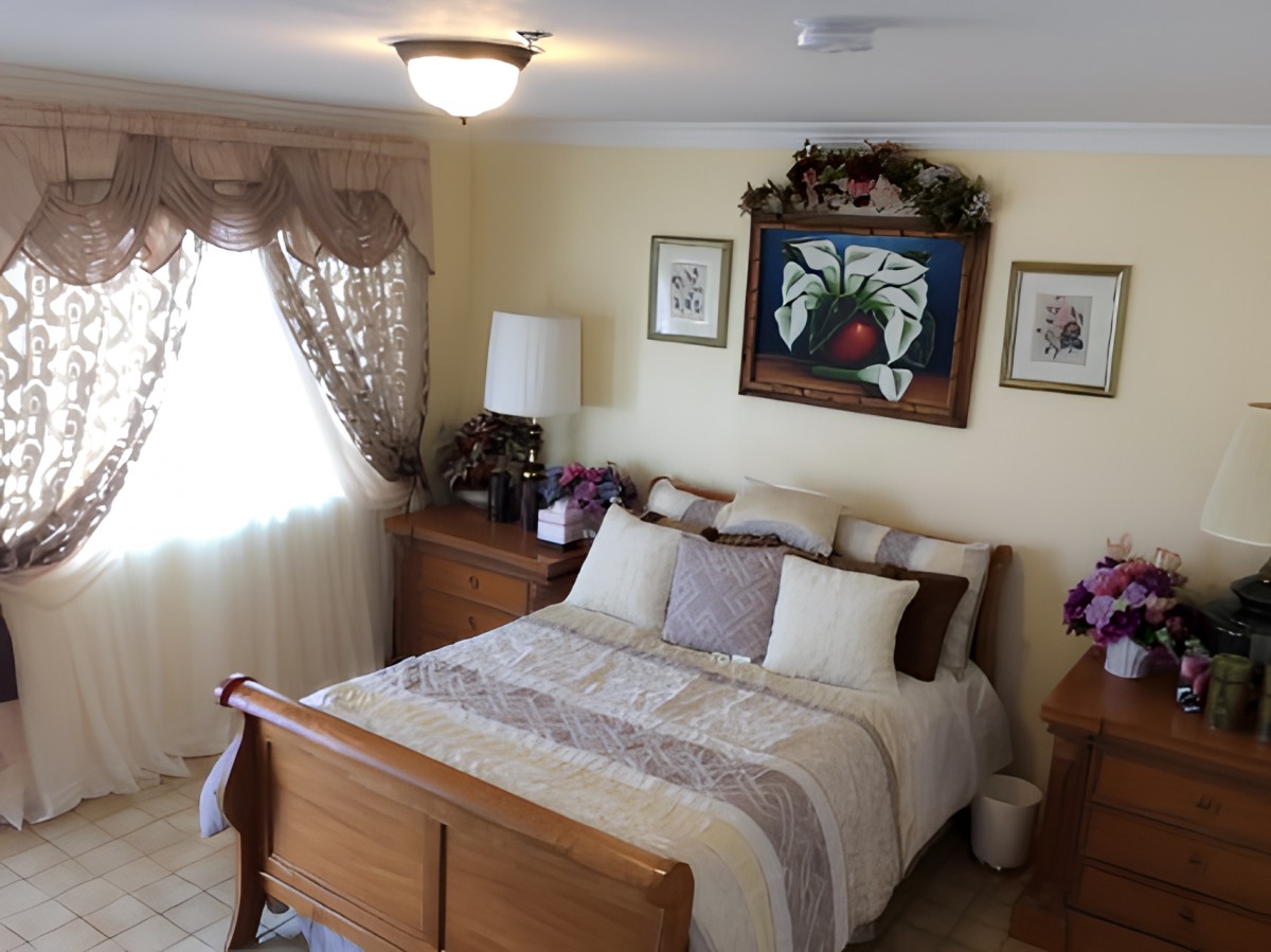 A cozy bedroom with a neatly made bed, wooden furniture, and decorative artwork on the wall.