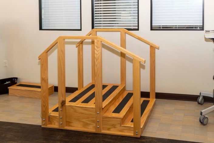 A small wooden staircase with handrails, used for physical therapy exercises indoors.