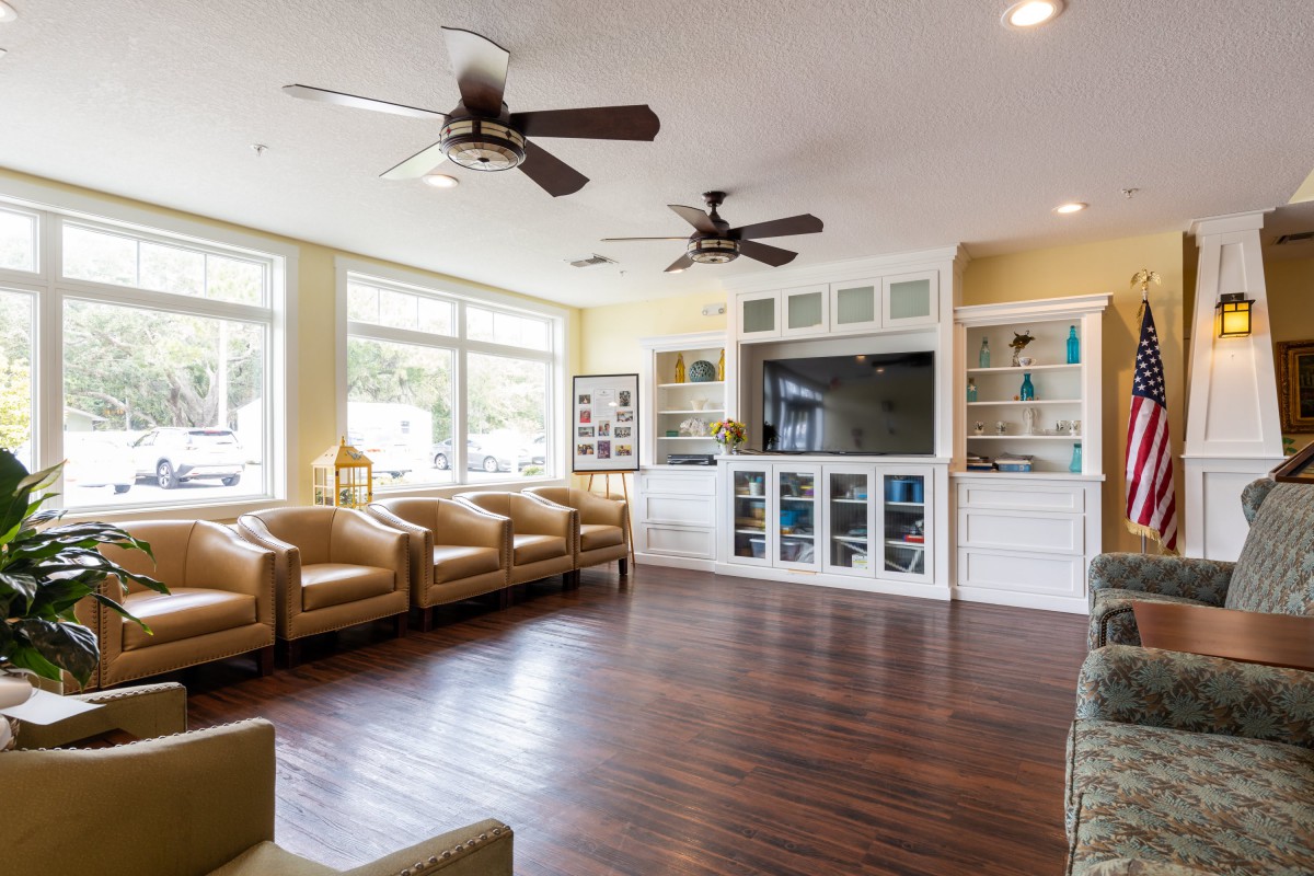 A spacious living room featuring comfortable seating, ceiling fans, and ample natural light from large windows.