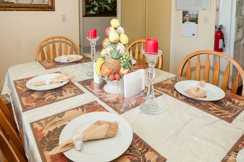 A well-decorated dining table set for a meal, featuring a centerpiece with decorative fruits and red candles.