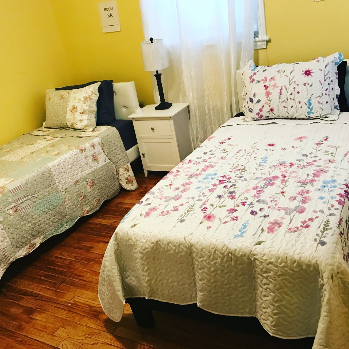 A cozy bedroom with two beds featuring floral bedding and yellow walls.