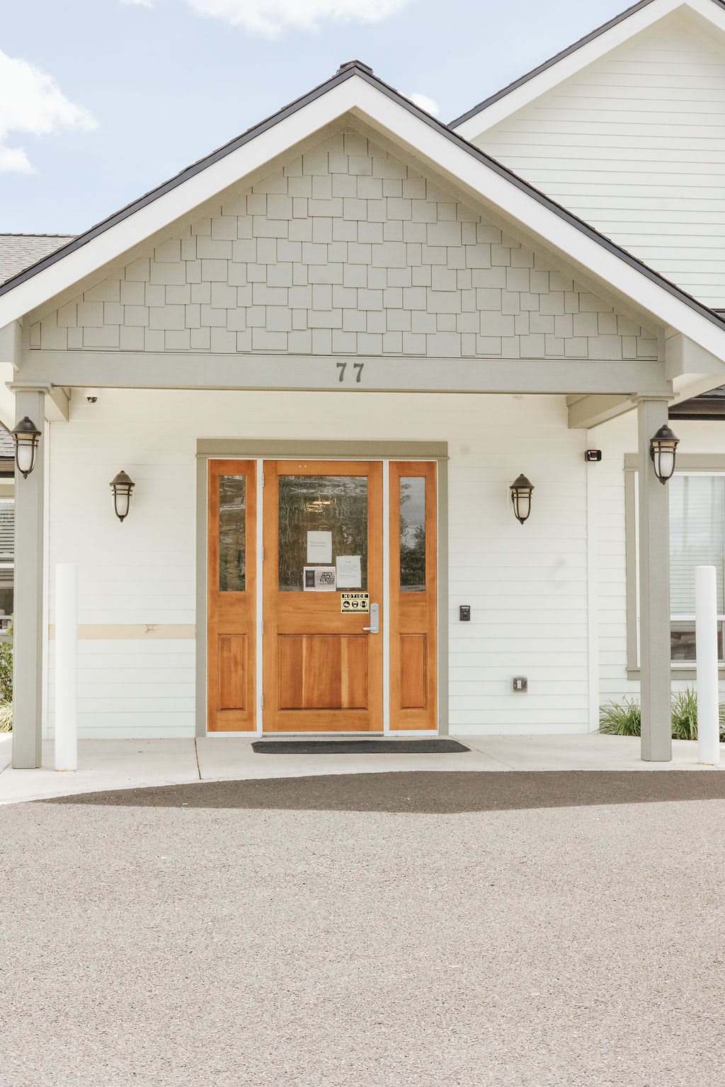 A white building entrance with a wooden door and decorative lighting.