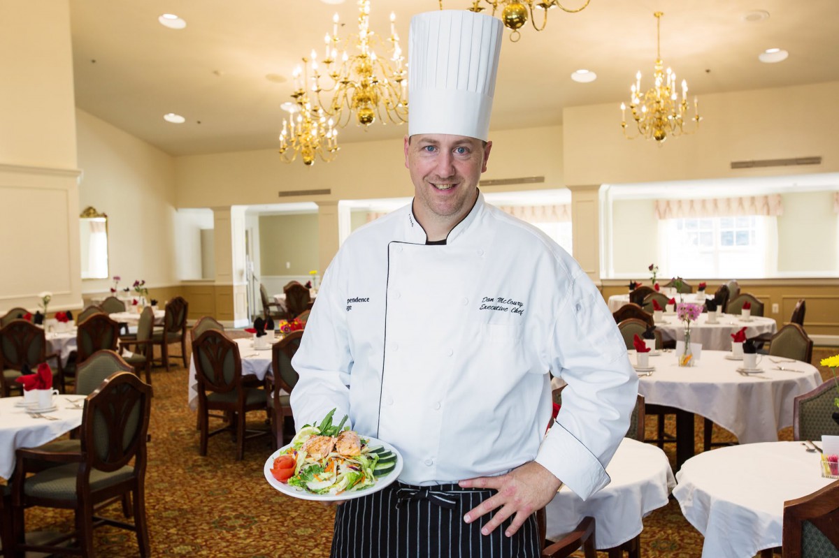 A chef proudly displays a beautifully plated dish in a restaurant setting.