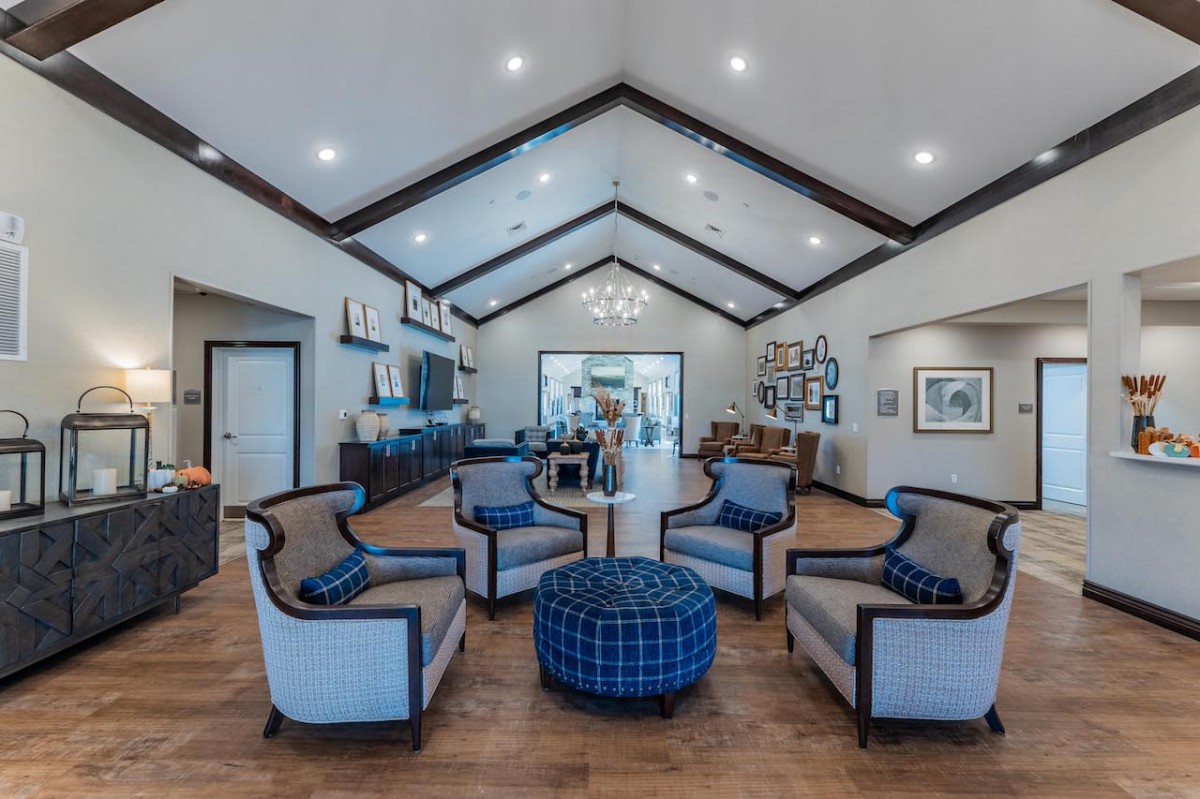 A spacious living room with modern furniture and a vaulted ceiling, featuring a central seating area and elegant lighting.
