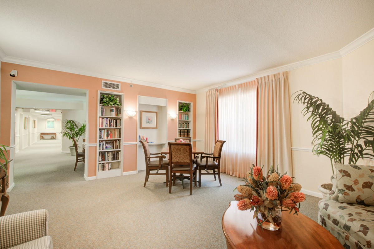 A cozy living and dining area with a table, chairs, and bookshelves, featuring soft peach-colored walls and floral decor.