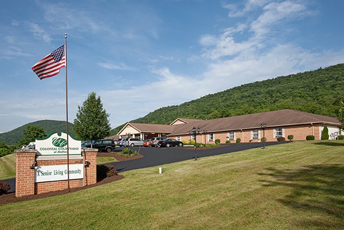A roadside motel with a parking lot and an American flag, set against a backdrop of rolling hills.