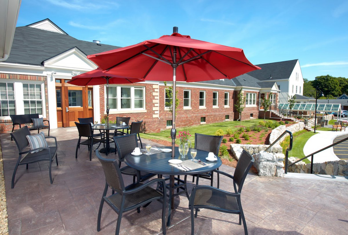 A sunny patio with dining tables and red umbrellas.