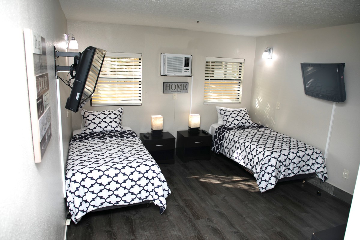 A modern bedroom featuring two twin beds with geometric patterned bedding, nightstands with lamps, and a wall-mounted television.
