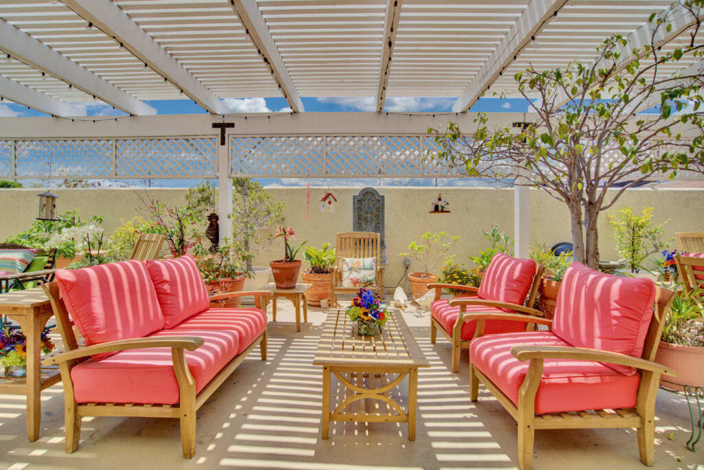 A cozy outdoor patio with red cushioned seating under a pergola, surrounded by plants.