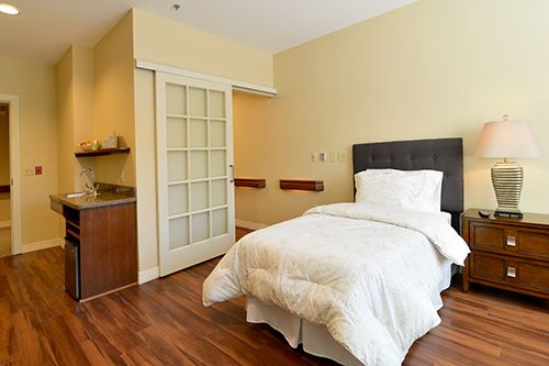 A cozy minimalist bedroom featuring a single bed with white bedding and sleek wooden flooring.
