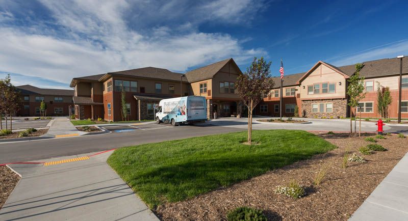 A moving truck is parked in front of a large residential building surrounded by a landscaped lawn on a partly cloudy day.