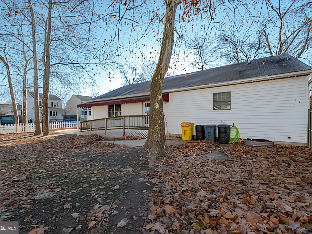 A house surrounded by trees with fallen autumn leaves covering the ground.