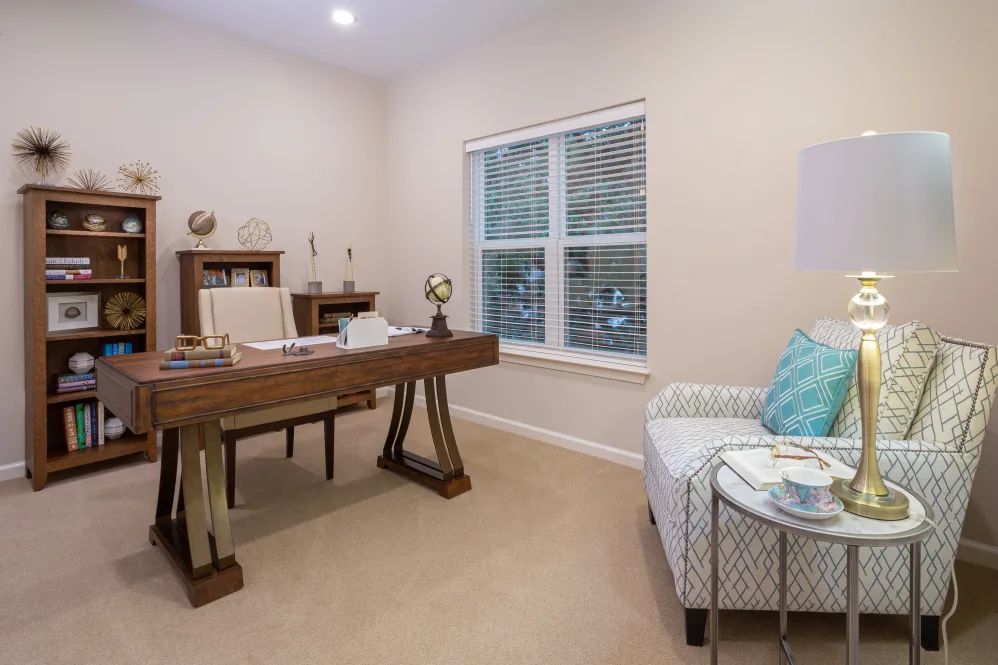 A neatly organized home office with a large wooden desk and an armchair by the window.