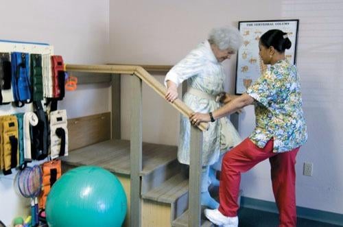 A caregiver assists an elderly person with physical therapy exercises.