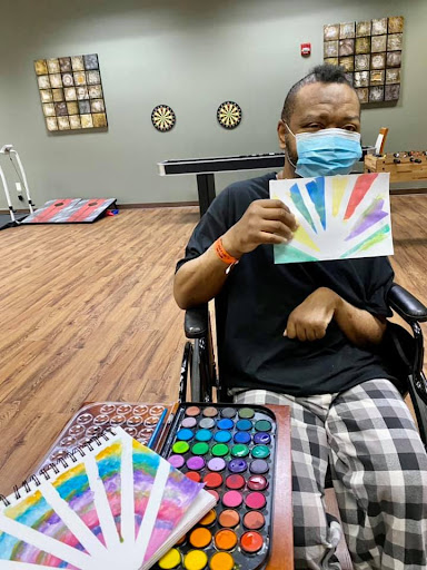 A person in a wheelchair showcases their colorful painting, highlighting the power of creative expression through art therapy.