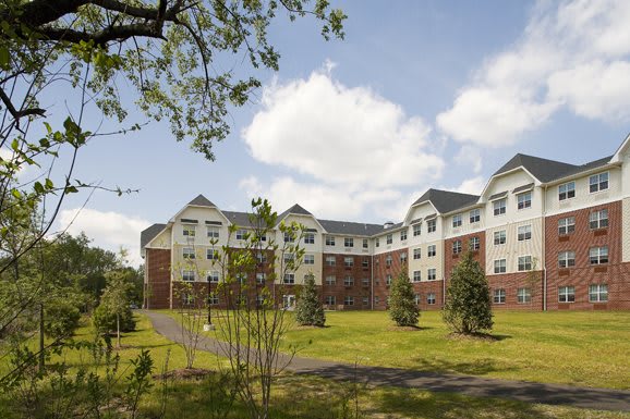 A large residential building with a well-maintained lawn and trees under a partly cloudy sky.