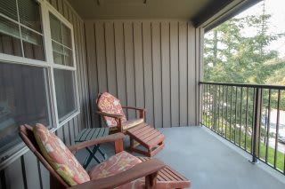 A cozy balcony with two cushioned wooden chairs and a scenic view.