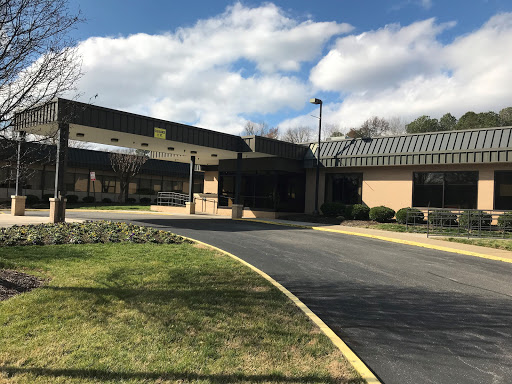 A view of the entrance to a hospitality building, set against a backdrop of clouds and greenery.
