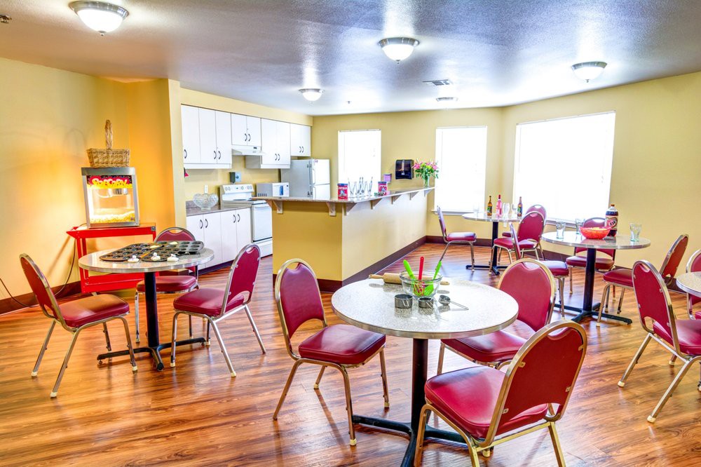 A cozy cafe with vibrant red chairs and round tables, featuring a small kitchenette and bright lighting.