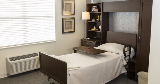 A well-organized room featuring a hospital bed with an over-bed table, a shelf, and a window.